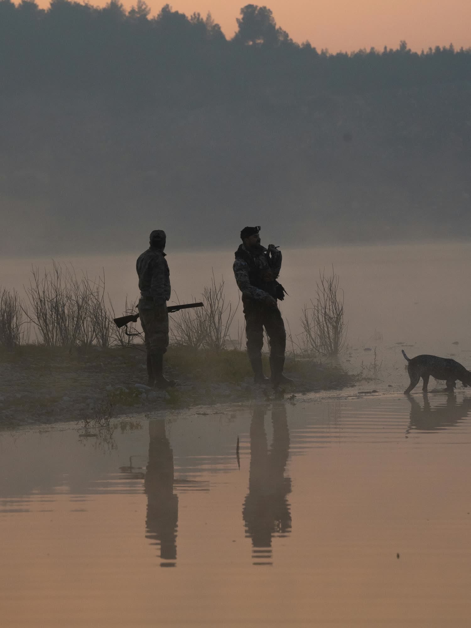 Falconer and shotgunner at first light over a Spanish lake