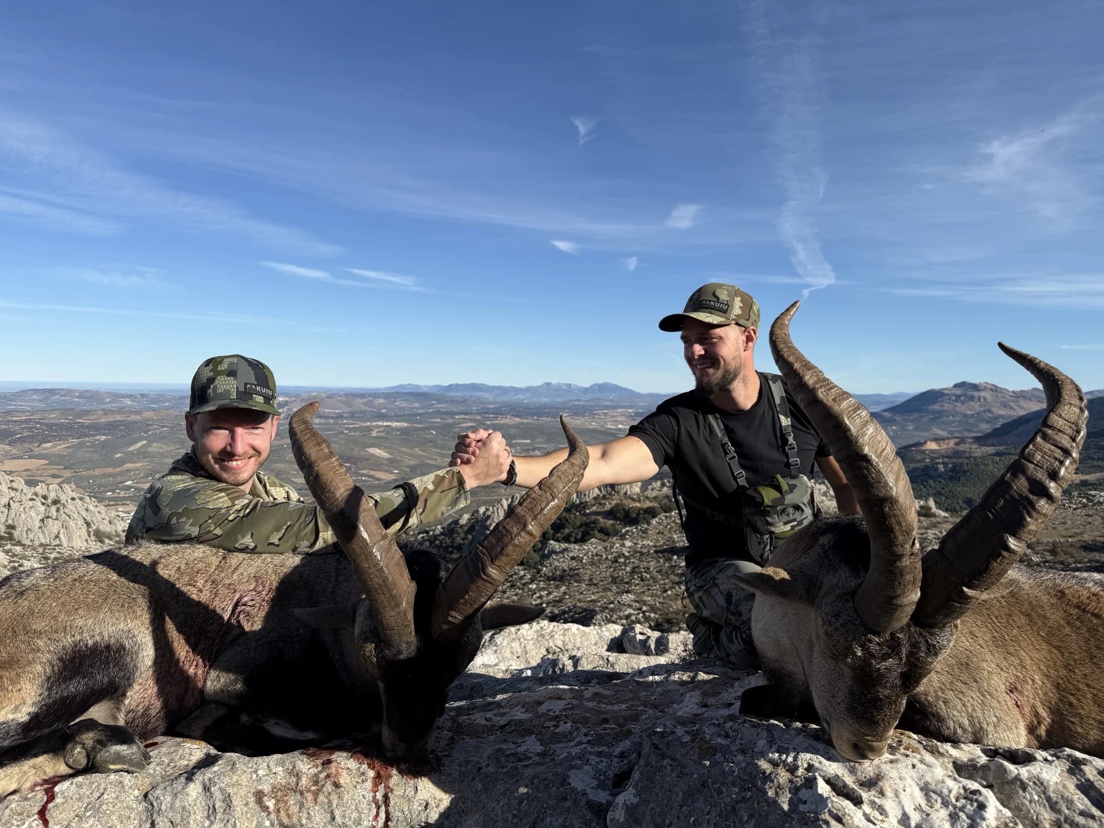 Two hunters clasping hands over their ibex on the ridge, Spain